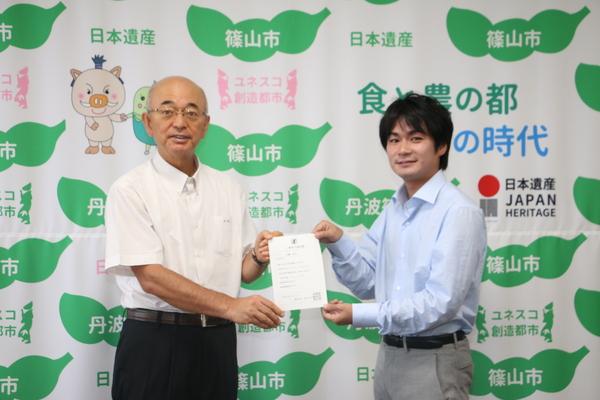 市長と川嶋さんが採用証明書を持って写っている記念写真
