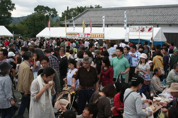 どてやき、お好み焼きなど書かれている屋台のテントの前を沢山の来場者達が歩いている写真