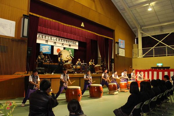 和太鼓の演奏が披露されているステージを椅子に座った在校生が見ている写真