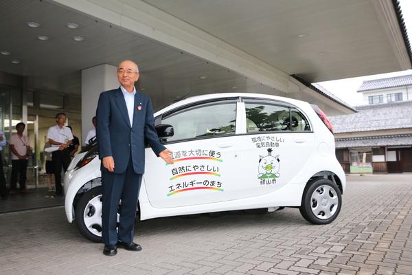 車体に「資源を大切に使う自然にやさしいエネルギーのまち」とゆるキャラ「まるいの」がラッピングされている 新しい公用車(電気自動車)と市長が一緒に写っている写真