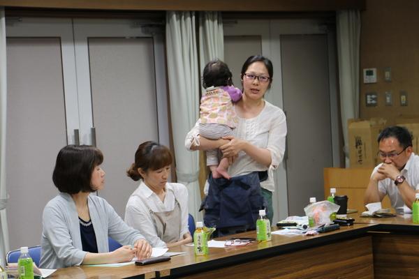 参加した眼鏡をかけた女性が立って乳幼児を抱っこしあやしながら話しをしている写真