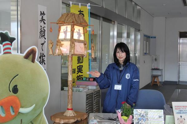 窓口に飾られている彫刻・デカンショ行燈を女性職員が手で案内している写真