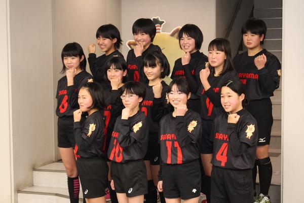 選抜で選ばれた12名の選手が、「まるいの」のイラストが肩にプリントされた黒色の同じユニホームを着て、左手でガッツポーズをして写っている集合写真