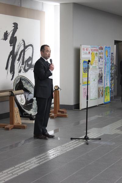 マイクをもって話す、スーツ姿の男性の写真