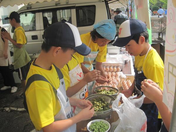 頭にバンダナや帽子を被ったエプロン姿の生徒たちが豆をむいている写真