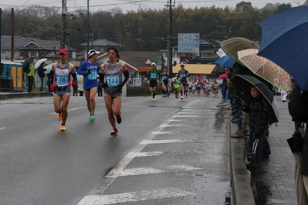 道路を走るランナーと傘をさして応援している写真