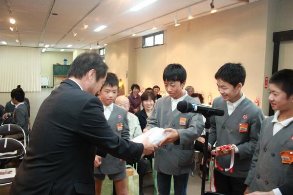 村雲小学校の代表の男子生徒4名が、出席者の前で、教育長賞の表彰を受けており、嬉しそうに記念品を受け取っている様子の写真