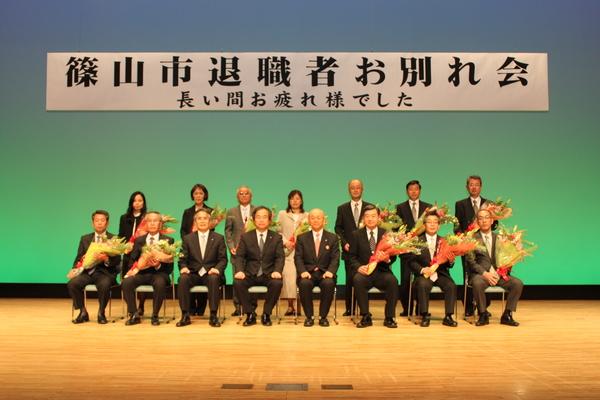 篠山市退職者お別れ会にて、花をもってなら並ぶ男女と市長と関係者の集合写真