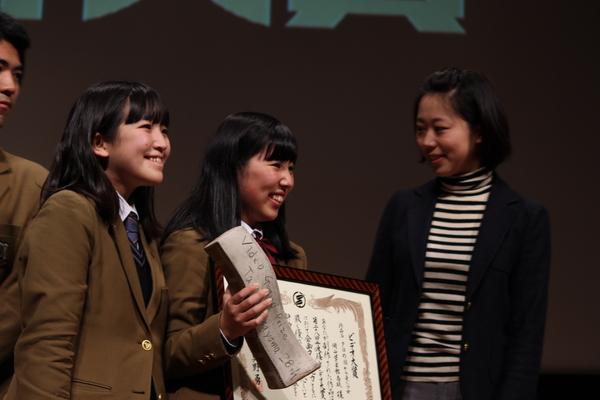 ビデオ大賞を受賞した岡山学芸館高校の女子生徒らが木のトロフィーと額に入った賞状を持って喜んでいる写真