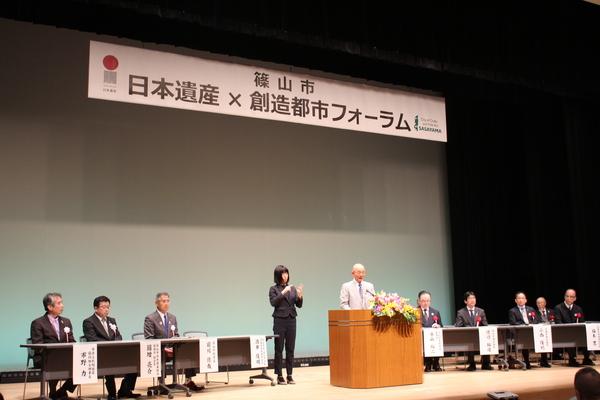 関係者が座る壇上にて、中央で市長が話をしているのを、女性が手話翻訳をしている写真