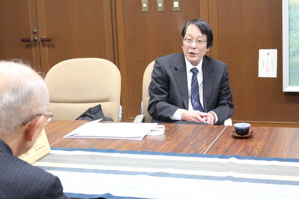 応接室でスーツをきた地主 力さんが椅子に座って市長と話をしている写真