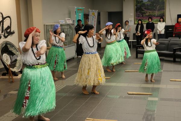 ロビーでフラダンスを踊っているココ ポスマンさんと5名の生徒の写真