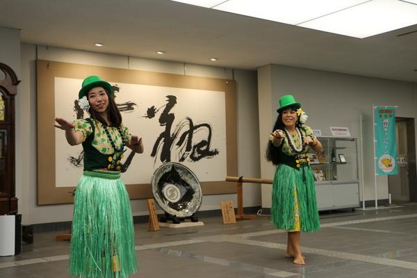 緑色の衣装と帽子を被り笑顔で踊っているココ ポスマンさんと生徒1名の写真