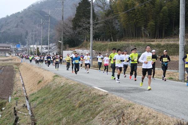 横には畑があり、まっすぐと縦に伸びた道をランナー達が走っている写真