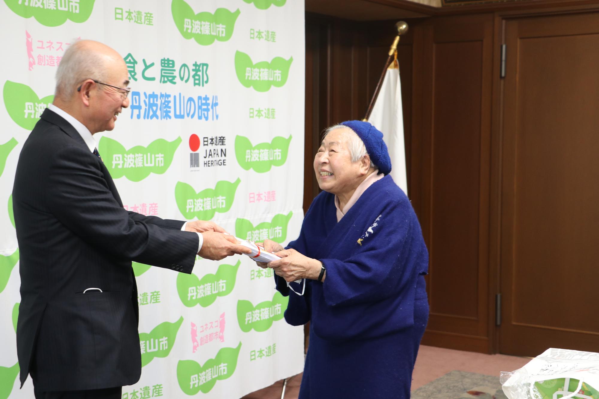 笑顔で寄付目録を市長に手渡す藤木さん