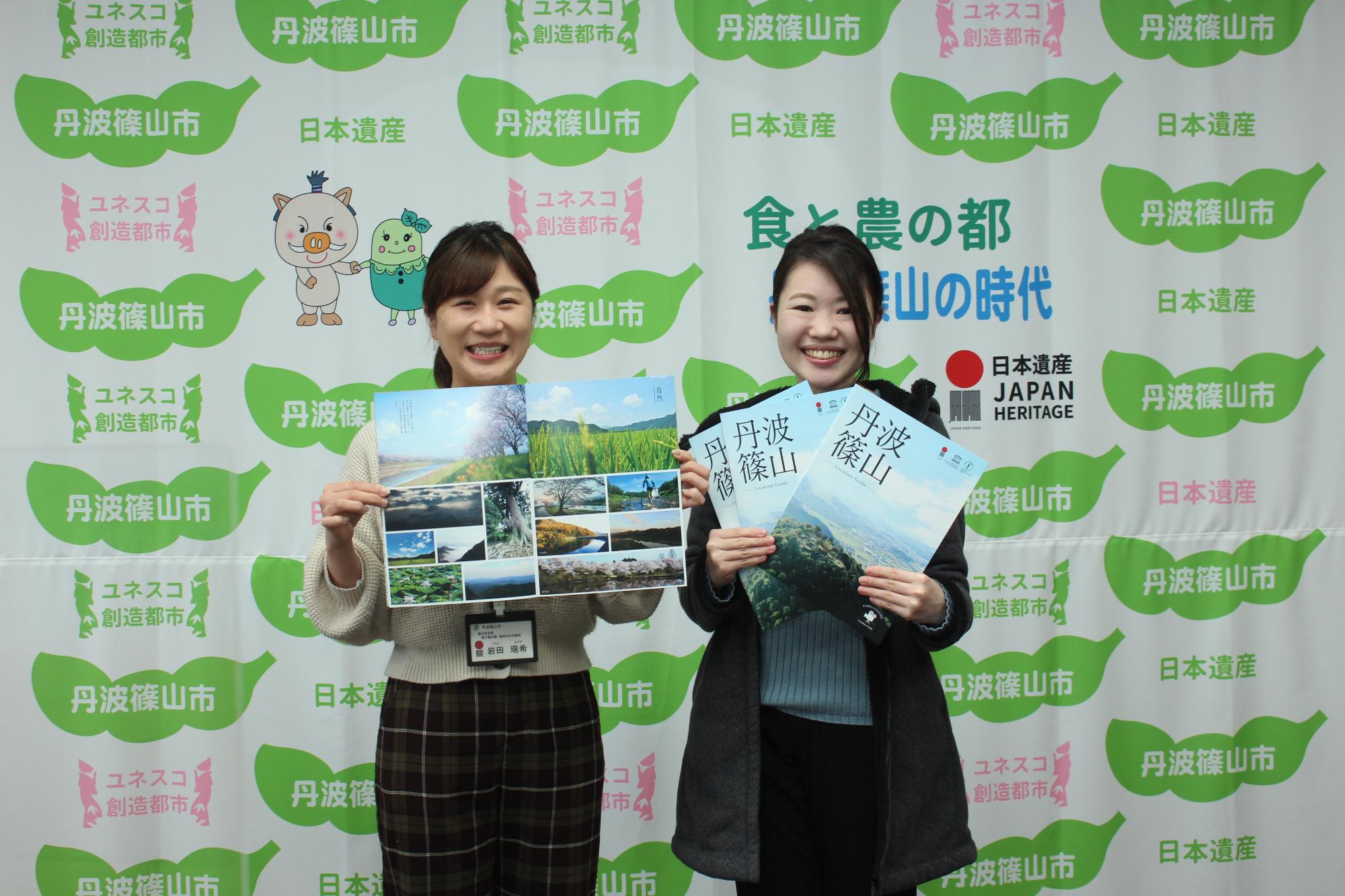 完成したロケーションガイドを二人の職員が手に持っている。