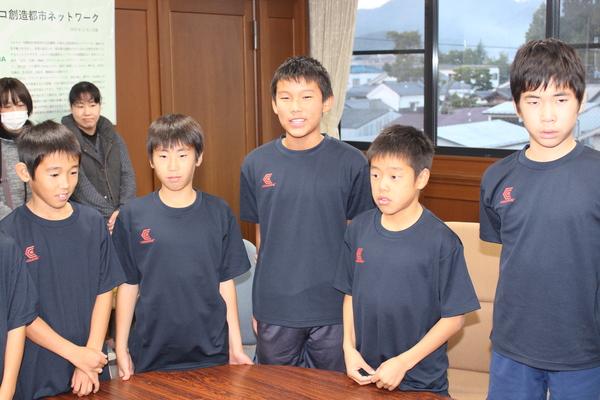 Tシャツ姿の少年5名が立っていて、その後ろに保護者の女性の方2名が立っている写真