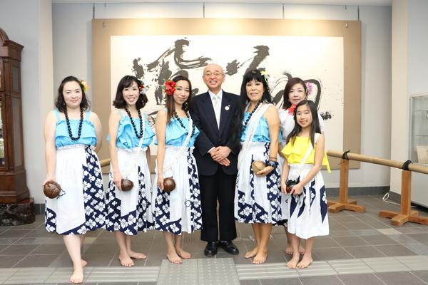 水色と白のスカートにハイビスカスの絵が載っている衣装を着た5名の生徒と黄色と大きなハイビスカスの絵が載っているスカートを履いた女の子の生徒が市長と笑顔で写っている写真