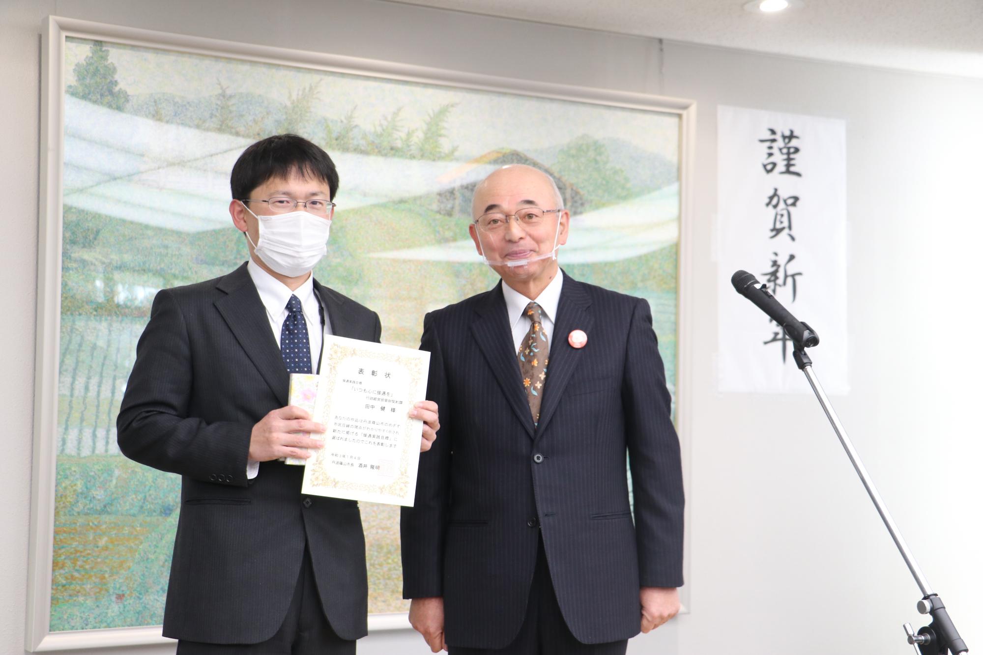 （左：代表して、表彰状と記念品を受け取る管財契約課田中係長、右：酒井市長）