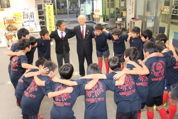 市長と寺本コーチとサッカークラブの少年たちが円陣を組んでいる写真