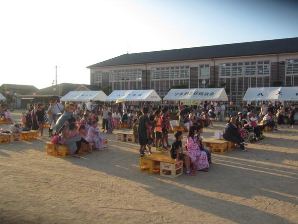 浴衣を着た子供たちやたくさんの人が、用意された席に座りにぎわう祭り会場の写真