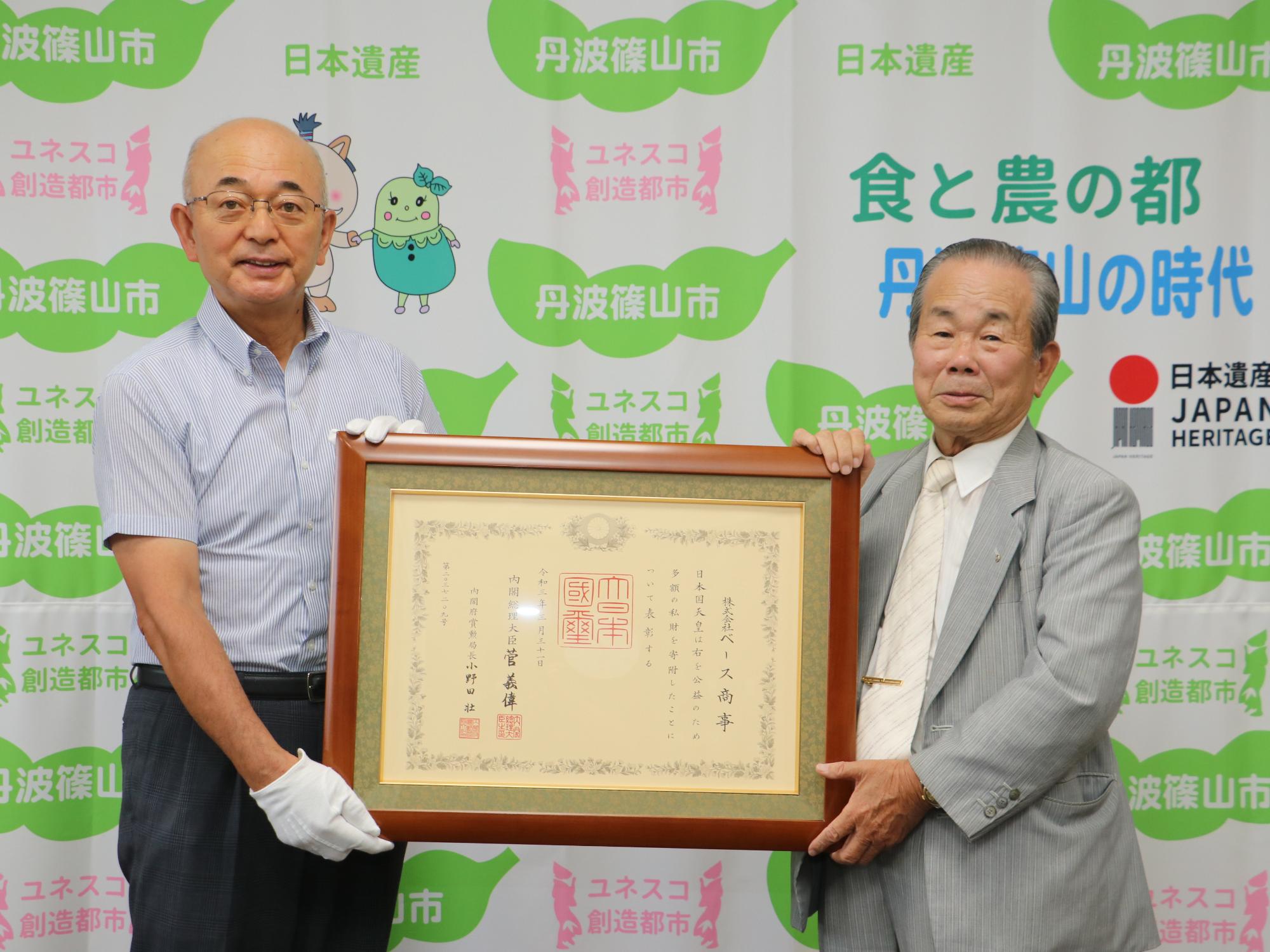 市長と男性が、紺綬褒章の額を一緒に持っている