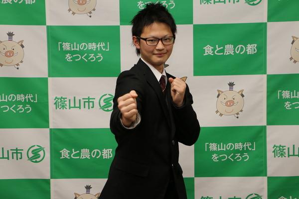 篠山市の文字が書かれた前で森本くんがカメラに向かってガッツポーズをとっている写真