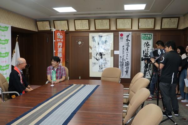 座って話している市長と原田さんを、カメラで撮っている写真