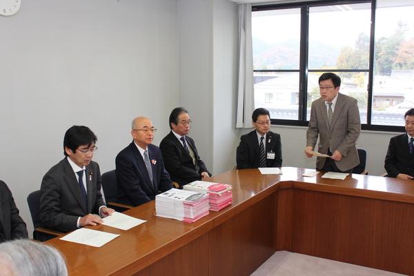 会議で、テーブルの市長の前に署名が置いてあり、圓増会長が立って話をしている写真