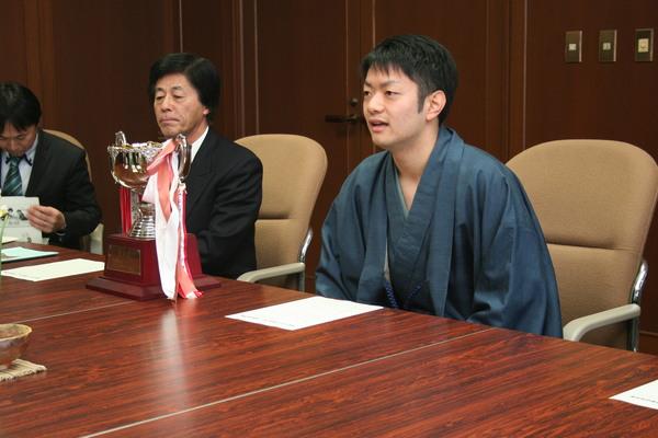 市長室にて、紺色の着物を着た岸田 諭さんが優勝のトロフィーを机の上に置き、椅子に座っている様子の写真