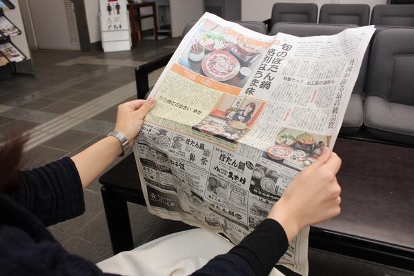 女性が「ぼたん鍋」の特集記事が大きく掲載されている新聞を両手に持っている写真