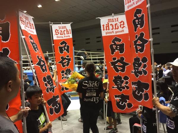 角谷 淳志と書かれた旗やTシャツを着た応援の方々を写した写真