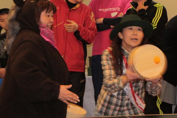 黒い帽子を被った女性が桶の底で卓球の玉を打ち返している写真