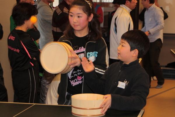 桶を持った子供が陣地に入ってきた卓球の玉を打ち返そうとしている写真