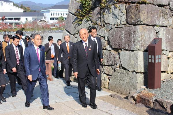 市長と菅官房長官が石垣の横の道を歩いている写真