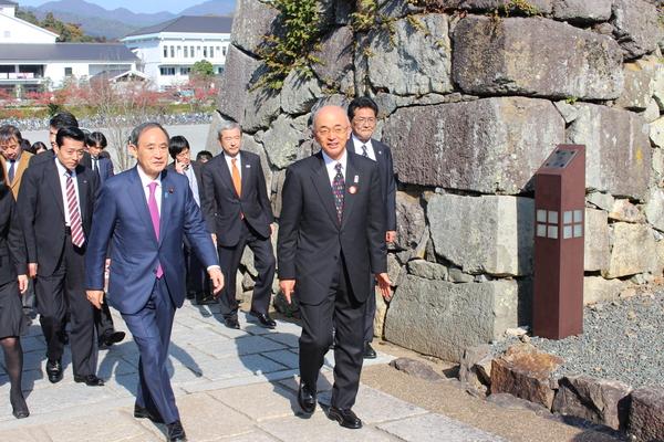 菅官房長官と市長が城の石畳を歩いている様子の写真