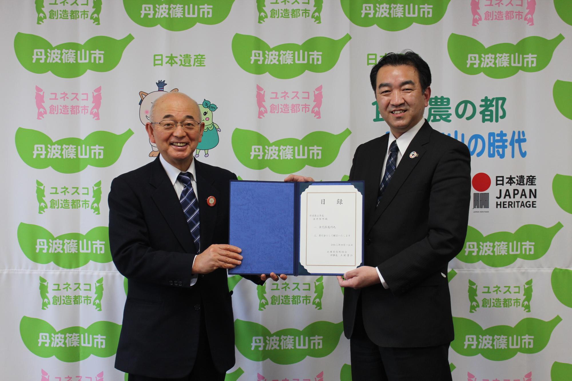 市長と兵庫県信用組合の方が一緒に目録を持って記念撮影している。