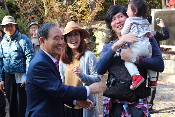菅官房長官が観光客の親子に声をかけ、赤ちゃんが泣き出してしまい、苦笑いをしている様子の写真
