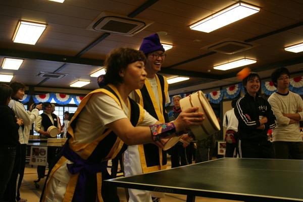 黄色の衣装を着た、男性が笑っていて、女性が桶を構えて打とうとしてる写真