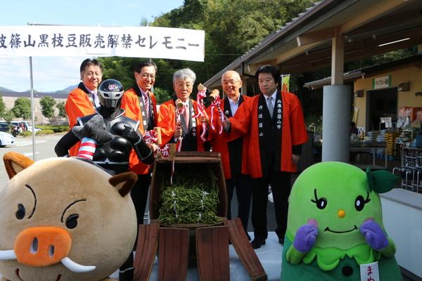 枝豆が入っている樽を前に赤い法被姿の市長らが小槌を持ちゆるキャラと一緒に写っている写真
