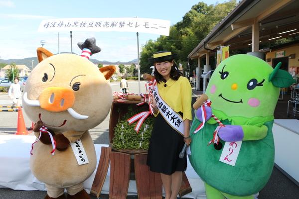 枝豆が入っている樽を前に丹波篠山観光大使の女性とゆるキャラが一緒に写っている写真