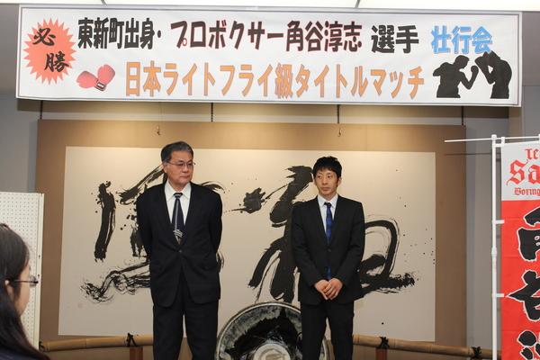 角谷 淳志（あつし）選手と関係者が隣にいて、日本ライトフライ級のタイトルマッチの看板が後ろにある写真