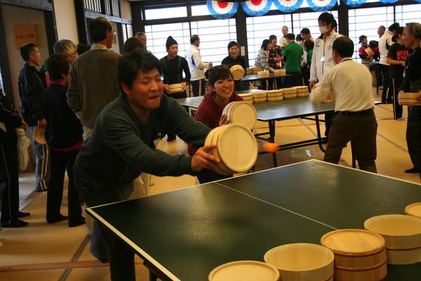 男性と女性がペアで桶を構えて球を打とうとしている写真