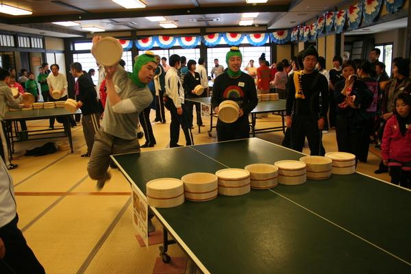 カッパの帽子をかぶった男性2人ペアの1人が大きく桶を上に持ち上げている写真