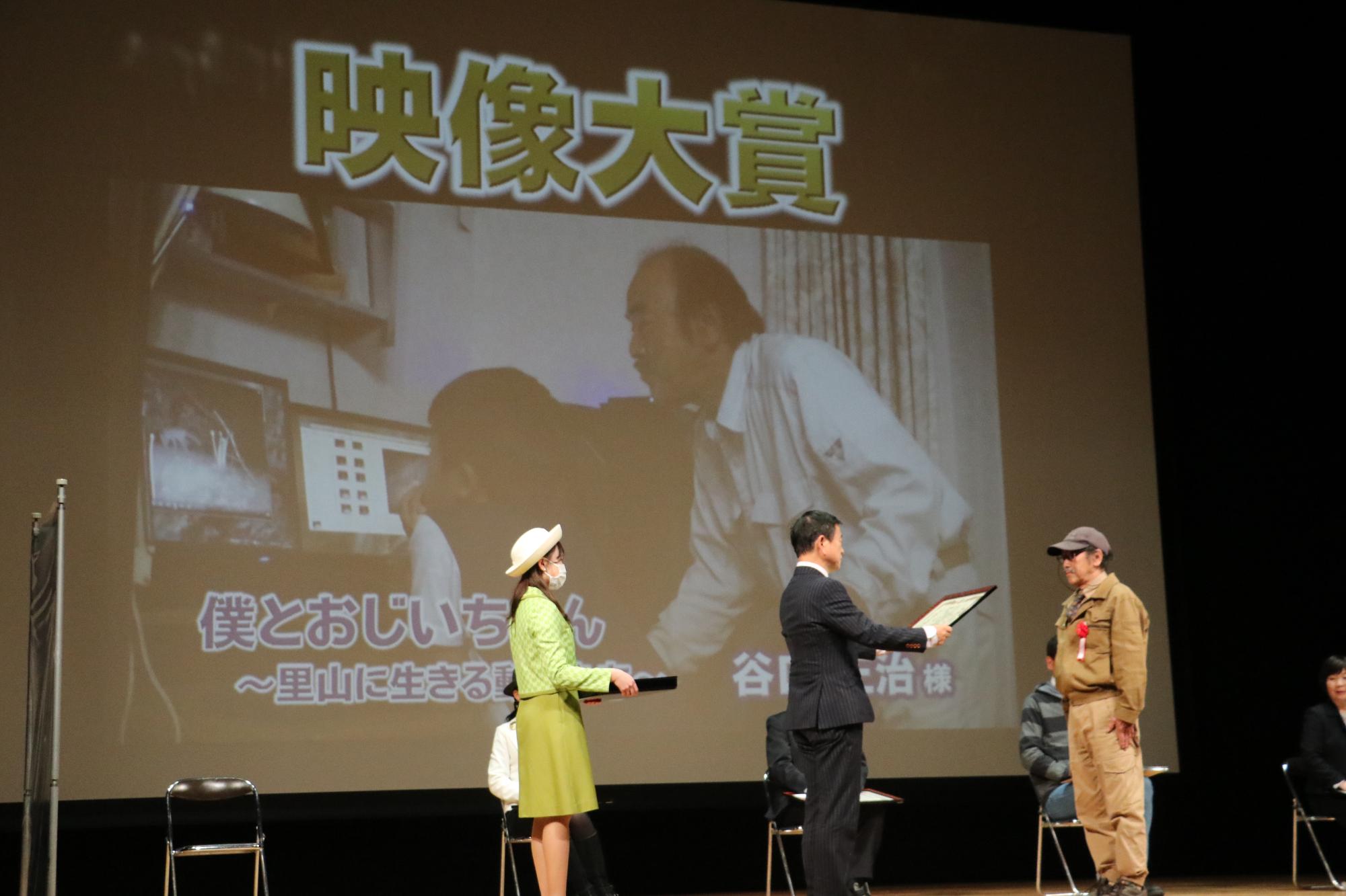 映像大賞を受賞された谷口さんが、舞台上で表彰状を授与されている