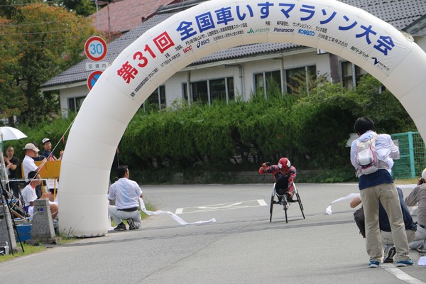 車いすマラソンで選手がガッツポーズしてゴールしている