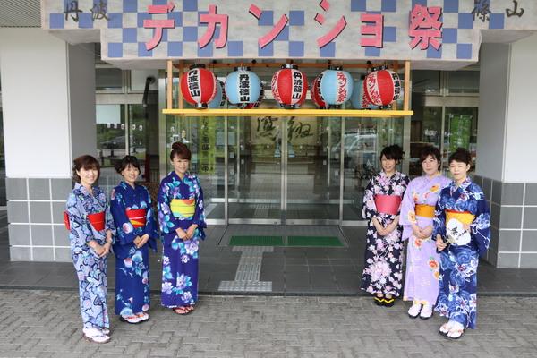 市役所の入口に「丹波篠山デカンショ祭」の看板と提灯が飾られており、両脇に浴衣姿の女性職員3名ずつ並んでいる写真