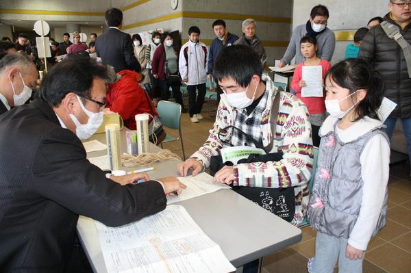 マスクの職員がマスクをした親子に説明している写真