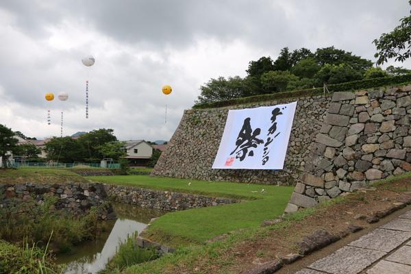デカンショ祭と書かれた旗が石壁に掛けられ、奥にアドバルーンが飛んでいる写真