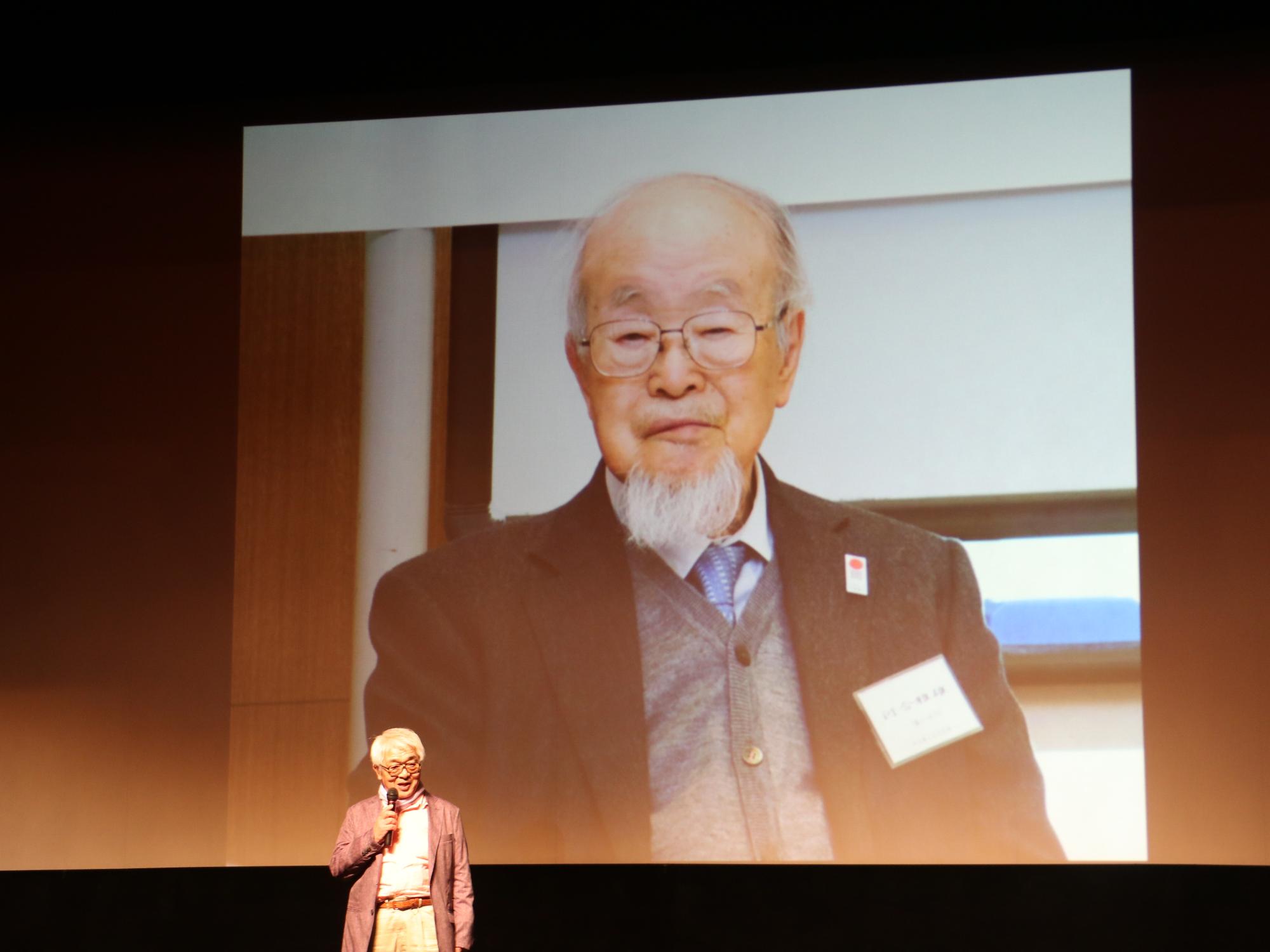 スクリーンいっぱいに雅雄先生の写真が写し出され、監督がマイクを持って話されている